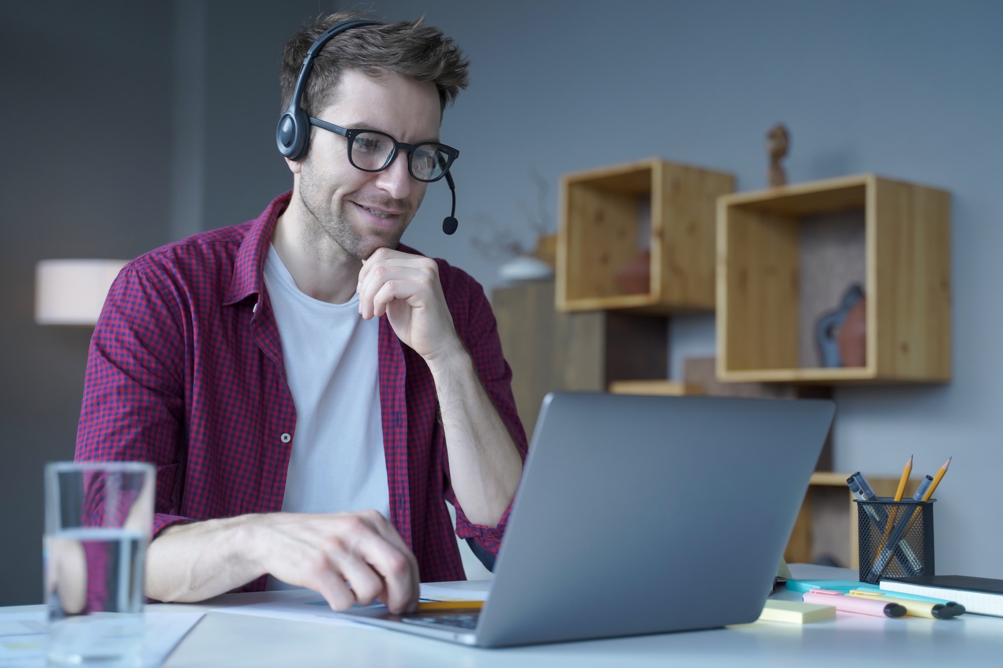 Smiling German guy sitting at home in wireless headset and taking part in online meeting